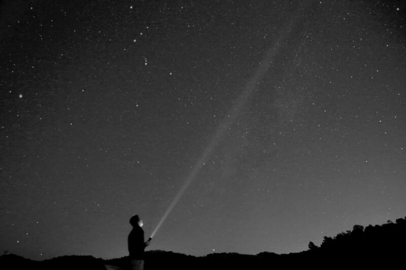 Josh pointing a beam of light from a torch into a starry night sky
